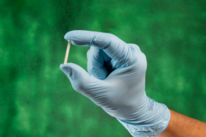 Gloved hand holding a contraceptive implant against a green background.
